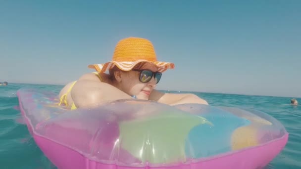 Attractive woman in an orange hat floats in the sea on an inflatable mattress — Stock Video