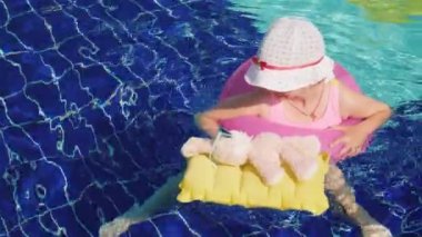 Komik kız bir mayo ve panama pembe tavşan havuzu güneş gözlüğü ile şişme daire banyoları. En sevdiğiniz oyuncak ile ortak dinlenme