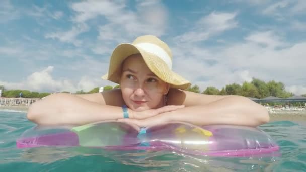 Uma mulher nova em um chapéu de palha está flutuando em um colchão inflável na costa — Vídeo de Stock