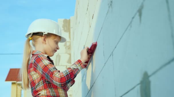 Un niño ingeniero en un casco mide la precisión de la mampostería de pared. Sueños de niños y conceptos de profesión — Vídeo de stock