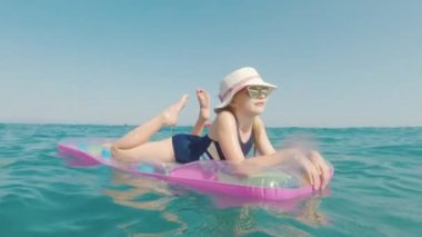 Bir kız bir şapka ve güneş gözlüğü bir şişme şişme denizinde yüzer. Mutlu tatil kavramı