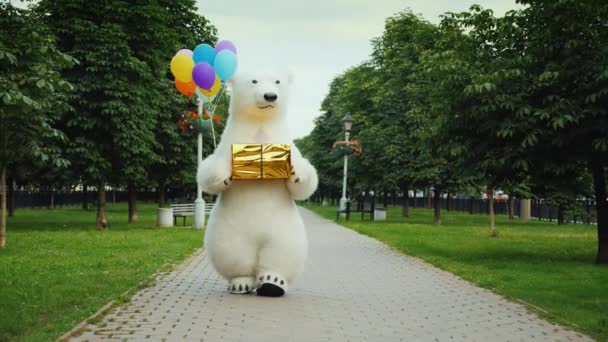 Een grote ijsbeer wandelingen in de straat, draagt ballonnen en een doos met een cadeau. Giften van de verjaardag en een koele partij concept — Stockvideo