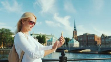 Bir genç kadın fotoğrafları kendini Stockholms şehir çizgi fon karşı bir akıllı telefon ile. Selfie Avrupa başkenti ve seyahat kavramında