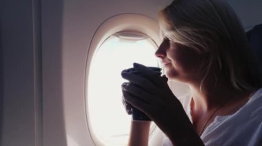 Bir kadın bir uçak kabin içinde kahve içiyor. Pencerenin kenarında oturur