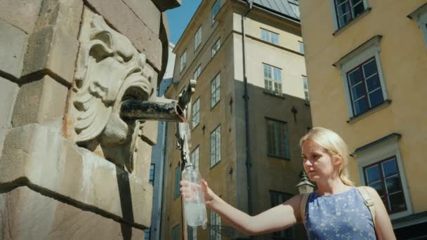 Een vrouw pakt water in een fles van een fontein in het centrale plein van Stockholm. Schoon drinkwater en goede ecologie — Stockvideo