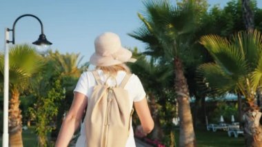 Bir turist onun arkasından pembe bir sırt çantası ile palmiye ağaçları avenue yürür. Dinlenme ve kavram yeni Gösterim