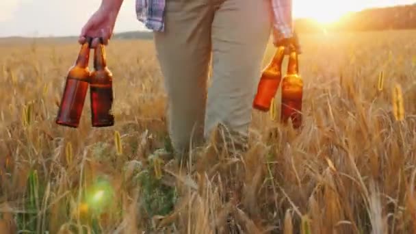 Una donna porta quattro bottiglie di birra fresca, cammina per il campo di grano. Mens concetto di fantasia — Video Stock