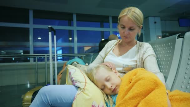 A woman is stroking a girl sleeping on her lap, sitting in the terminal of the airport. Flight delay concept — Stock Video