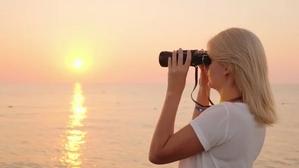 Jovem atraente olha através de binóculos ao nascer do sol sobre o mar. Romance e aventura — Fotografia de Stock