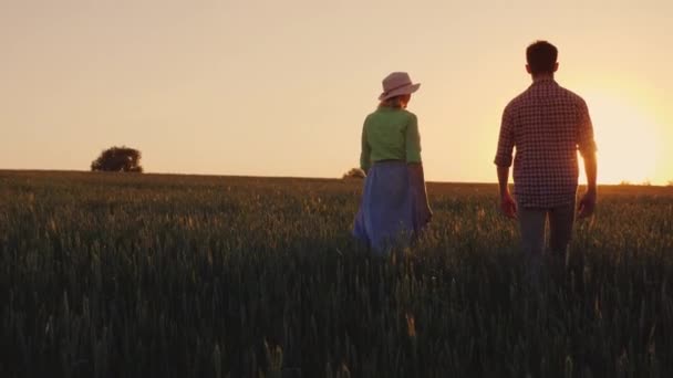 Una familia de agricultores camina por el campo de trigo hasta el horizonte, donde el sol se pone — Vídeo de stock