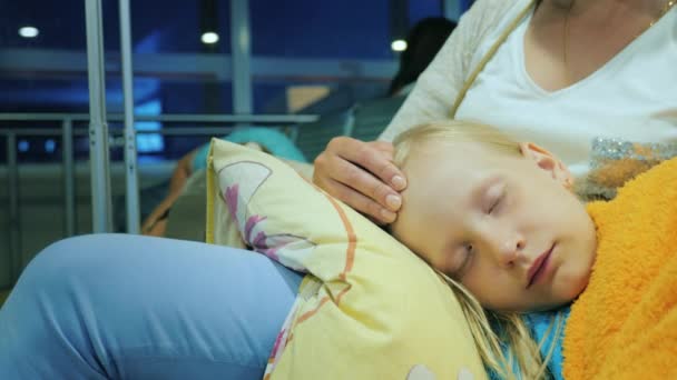 Een vrouw is een meisje dat slapen op haar schoot, zittend in de terminal van de luchthaven aaien. Vlucht vertraging concept — Stockvideo