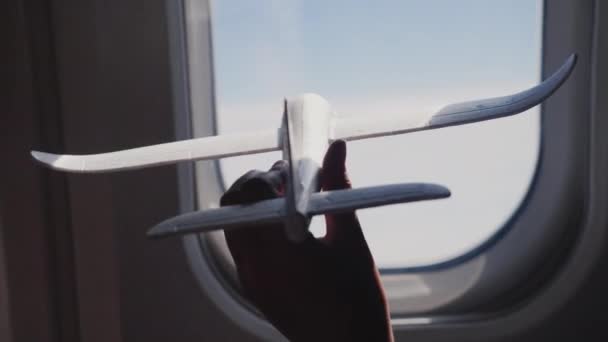 Une main enfantine tient un avion jouet sur le fond de la fenêtre de l'avion. Rêves et voyages avec enfants concept — Video