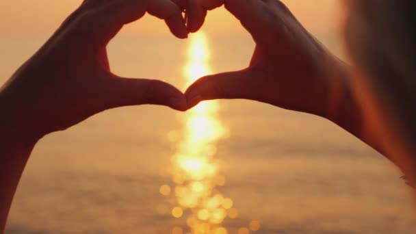 Ženské ruce ukazují tvar srdce nad mořem, kde vychází slunce. Krásná romantická scéna