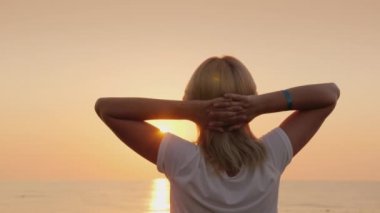 Genç Sarışın turist şafak üzerinde sahil karşılar, rahatlatır, sessizlik sahiptir. Arkadan görüntülemek