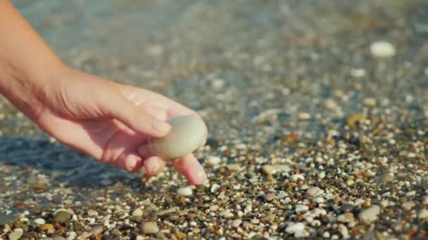 Una mano femminile tiene un sassolino sullo sfondo del surf . — Video Stock