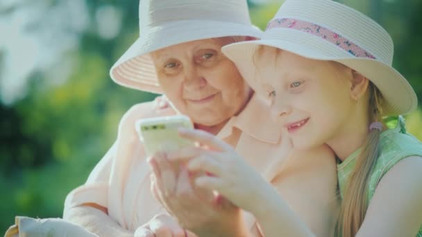 Egy lány azt mutatja, hogy a nagymamája, játszik egy smartphone. Úrvacsora generációk koncepció — Stock videók