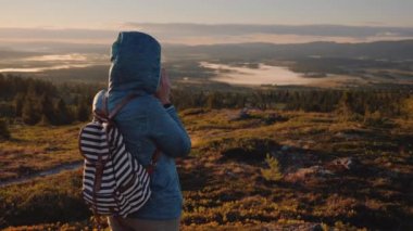 Kapüşonlu adam dağın, ellerini ısınma bir kupa sıcak kahve içme dinleniyor. Norveç'te seyahat