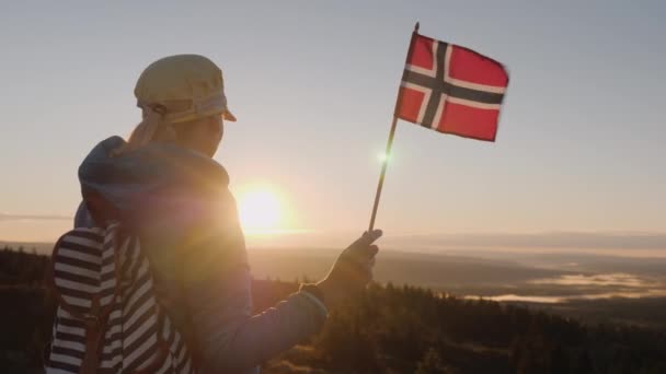 Мандрівник з прапором Норвегії в руці зустрічає Схід сонця на вершину гори. Користується красивою природою суворого краю — стокове відео