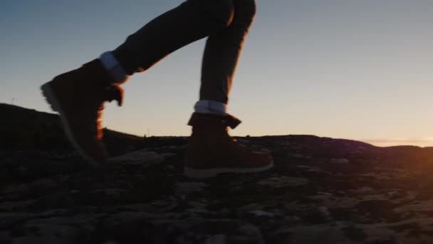 Les jambes en bottes de trekking longent la crête de la montagne sur fond de soleil levant. Concept de voyage et d'aventure — Video