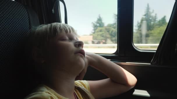 A rapariga está a dormir junto à janela no banco de trás do carro. Uma viagem tediosa com uma criança — Vídeo de Stock