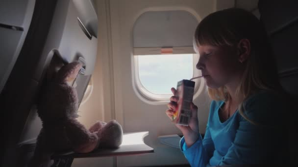 La niña en la cabina del avión - bebiendo jugo del tubo, con su juguete volador - una liebre — Vídeos de Stock