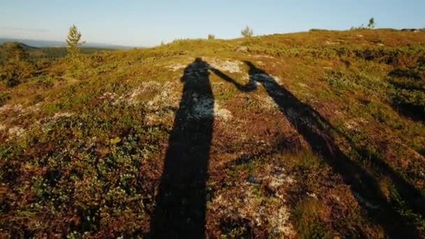 Las sombras de dos viajeros caminan por el terreno montañoso, tomados de la mano. Estilo de vida activo — Vídeo de stock