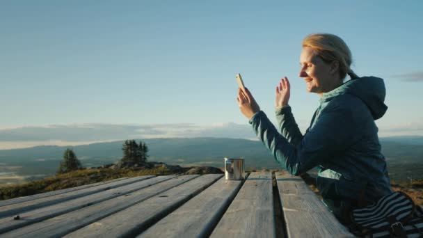 Cestovatel se mluví na video chatu. Sedí u stolu vysokou v horách proti pozadí norský malebné krajiny. Daleko od civilizace — Stock video