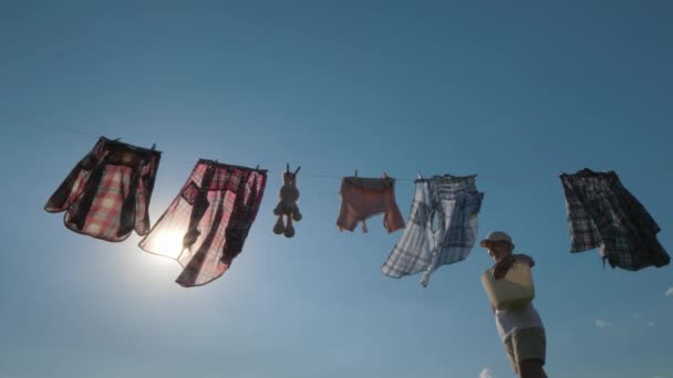 Een vrouw met een mand eruit opknoping natte kleren aan een touw — Stockvideo