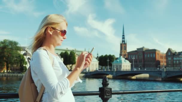 Eine junge frau benutzt ein smartphone vor dem hintergrund der stadtlinie von stockholm, schweden. immer in Kontakt — Stockvideo