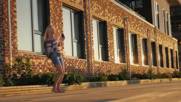 一个无忧无虑的中年妇女听音乐和舞蹈在街道附近的一个美丽的砖砌建筑 — 图库视频影像