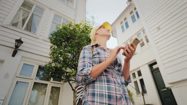 Женщина использует приложение map на смартфоне, стоящем среди старых деревянных домов. Озил, Норвегия — стоковое видео