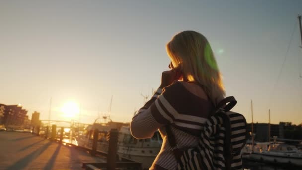 Una mujer camina por el muelle al atardecer, escuchando música con auriculares. La ciudad de Bergen en Noruega — Vídeo de stock