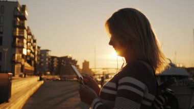 Kulaklıklar bir kadında bir akıllı telefon arka plan özel yat iskelede kullanır. Gün batımında, güneş güzel bu aydınlatır.