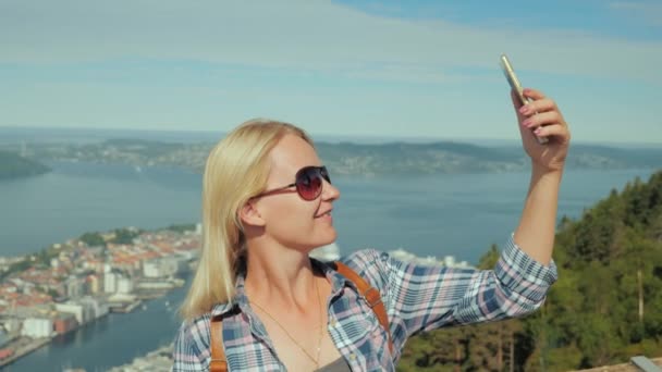 Женщина-туристка фотографирует себя на фоне города Берген в Норвегии — стоковое видео
