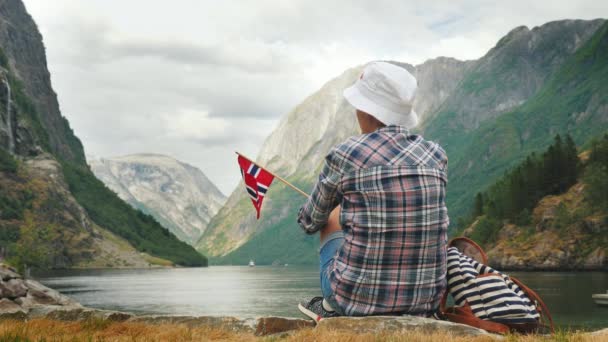 Una donna con la bandiera della Norvegia in mano ammira il bellissimo fiordo. Turismo in Scandinavia concetto — Video Stock