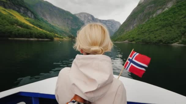 Una mujer con la bandera de Noruega se para en la nariz de un crucero, navega en un pintoresco fiordo en Noruega — Vídeos de Stock