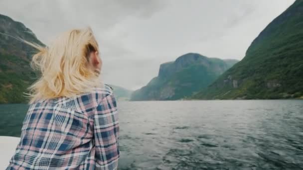 Romantyczna kobieta na dziobie statku, płynąc wzdłuż fiordu piękne. Wiatr wieje w jej włosy — Wideo stockowe