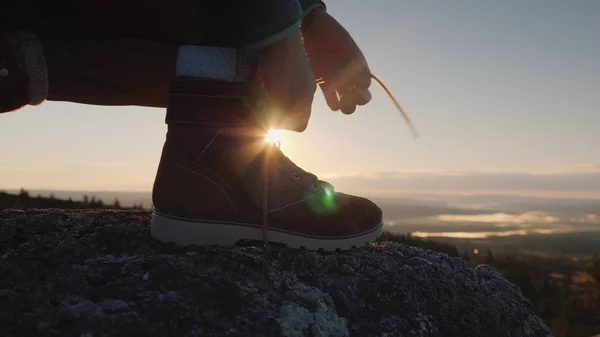 De reiziger verbindt de schoenveters over het bijhouden van de schoenen. Op de top van de berg tegen de achtergrond van de rijzende zon. Het begin van een grote reizen-concept — Stockfoto