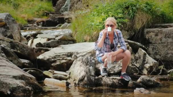 Egy nő a tiszta víz, a patak felvett italok. Norvégia, vízesés Tvindefossen — Stock videók