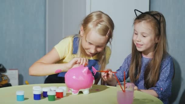 Duas meninas namoradas pintar um porquinho banco juntos, divirta-se — Vídeo de Stock