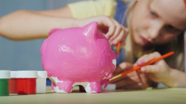 Children cheerfully paint piggy bank. Happy childhood concept clipart