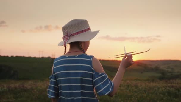 Ein lustiges kleines Mädchen mit Strohhut und Zöpfen startet ein Spielzeugflugzeug in den Himmel. — Stockvideo