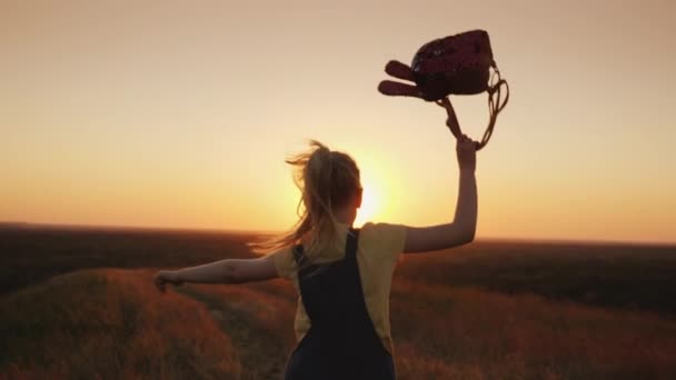 Una ragazza con una borsetta corre leggera e spensierata al sole che sorge. Felice estate infanzia e concetto di vacanza — Video Stock