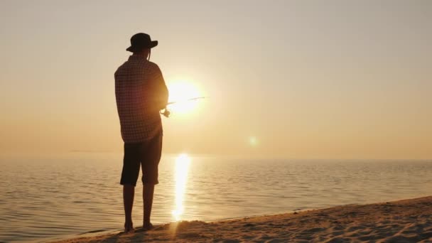 Um jovem está pescando na margem de um lago pitoresco ao pôr do sol — Vídeo de Stock