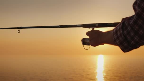 Een man is de visserij op de kust, in het kader van dat de armen worden gedraaid door een spool handvat op het spinnen — Stockvideo