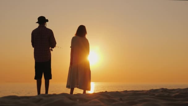 Ein Mann angelt am Strand, seine schwangere Frau steht in der Nähe — Stockvideo