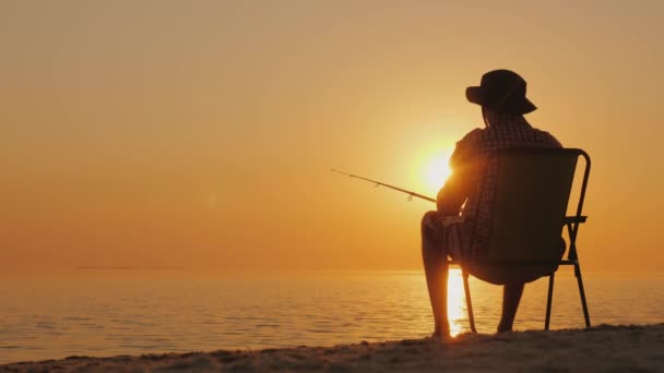 Ένας νεαρός άνδρας κάθεται στην παραλία, ψάρεμα. Χαλαρώνοντας στην ύπαιθρο — Αρχείο Βίντεο