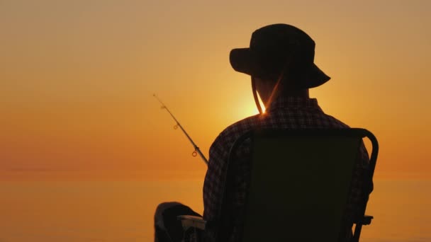 Achteraanzicht - een man zittend op de seashore, vissen met een hengel — Stockvideo