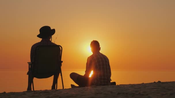 Twee vrienden rusten op de oever van het meer op zonsondergang, fishing. Vriendschap en ontspanning in de open lucht — Stockvideo