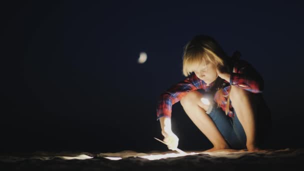 Дівчина з ліхтариком в руці шукає щось на пляжі в темряві. Дослідження та концепція пригод — стокове відео